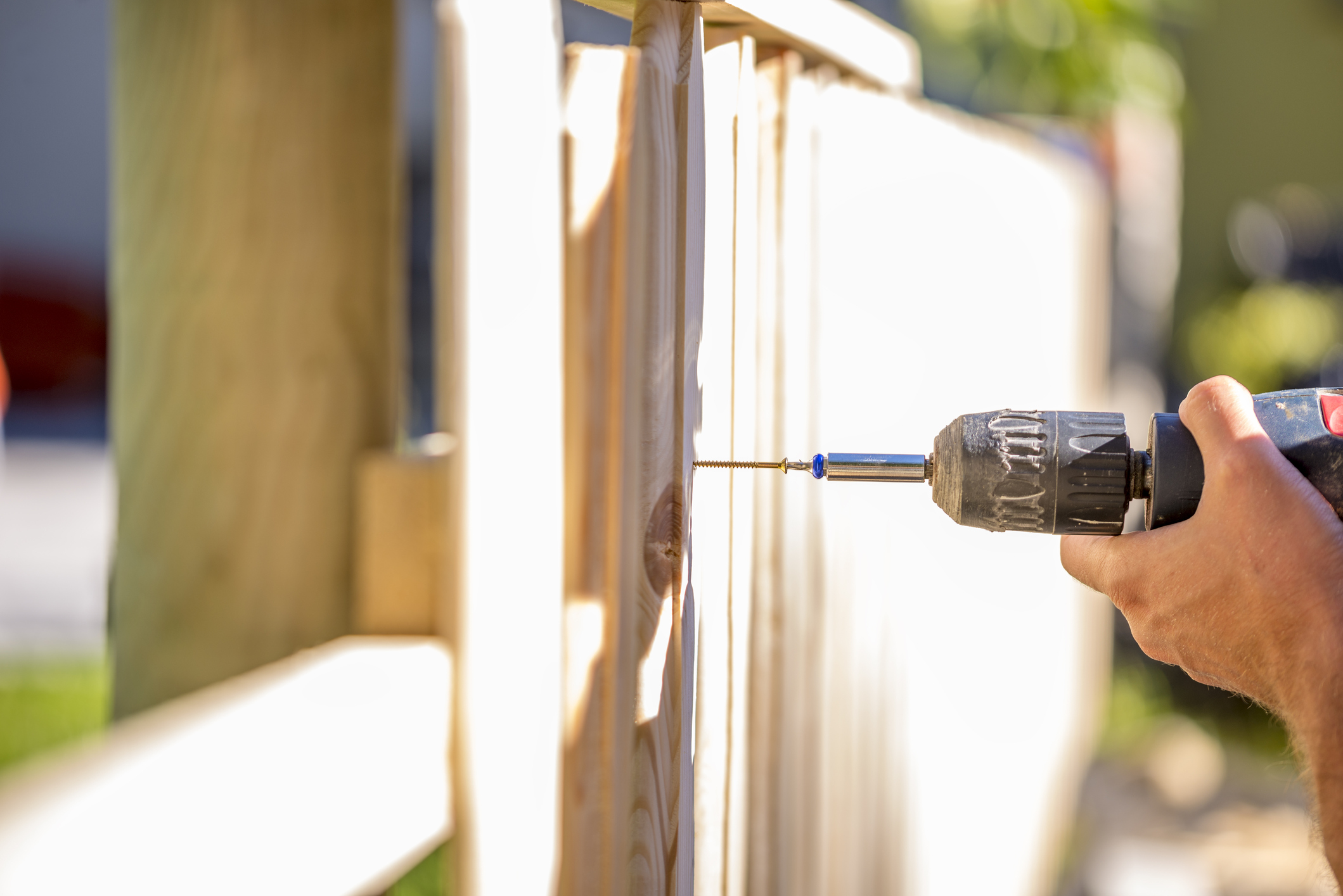 Person holding a drill, drilling into a wooden fence