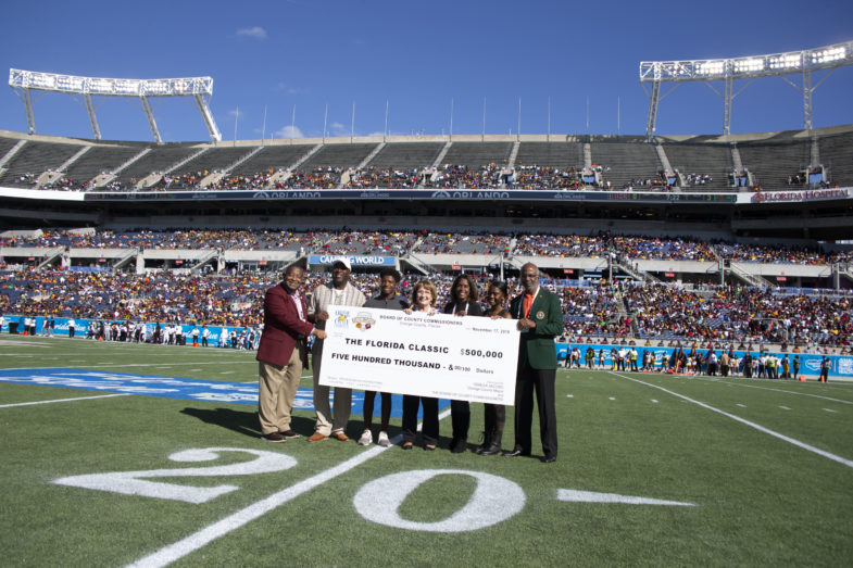 Mayor Jacobs and a small group hold a life-size check in the middle of a football field