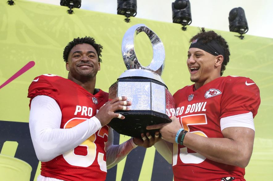Two NFL players from the Jets football team smiling as they hold the NFL Pro Bowl Championship trophy.