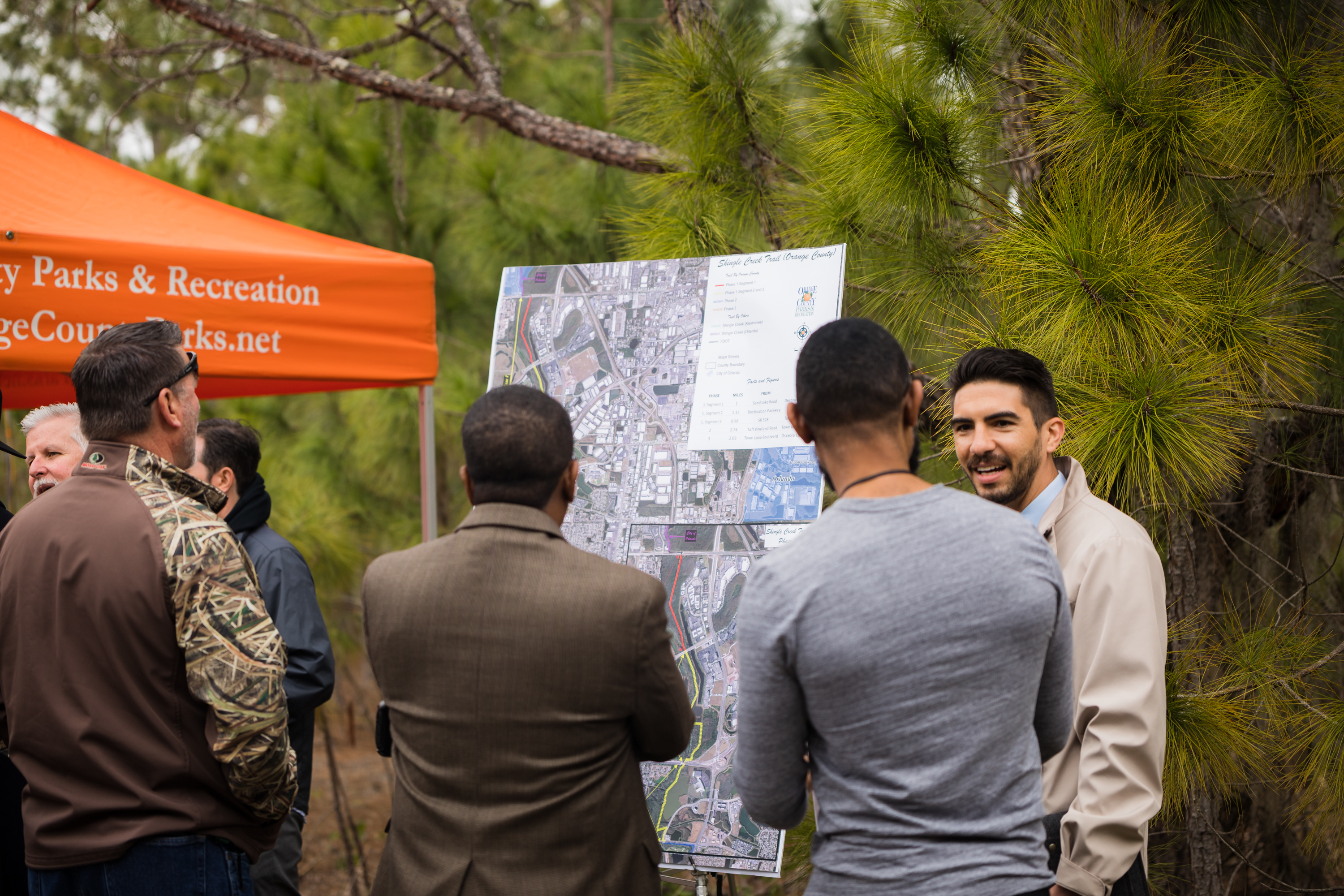 Four residents and community leaders, all men, standing in front of a large map. They are outside on an overcast day.