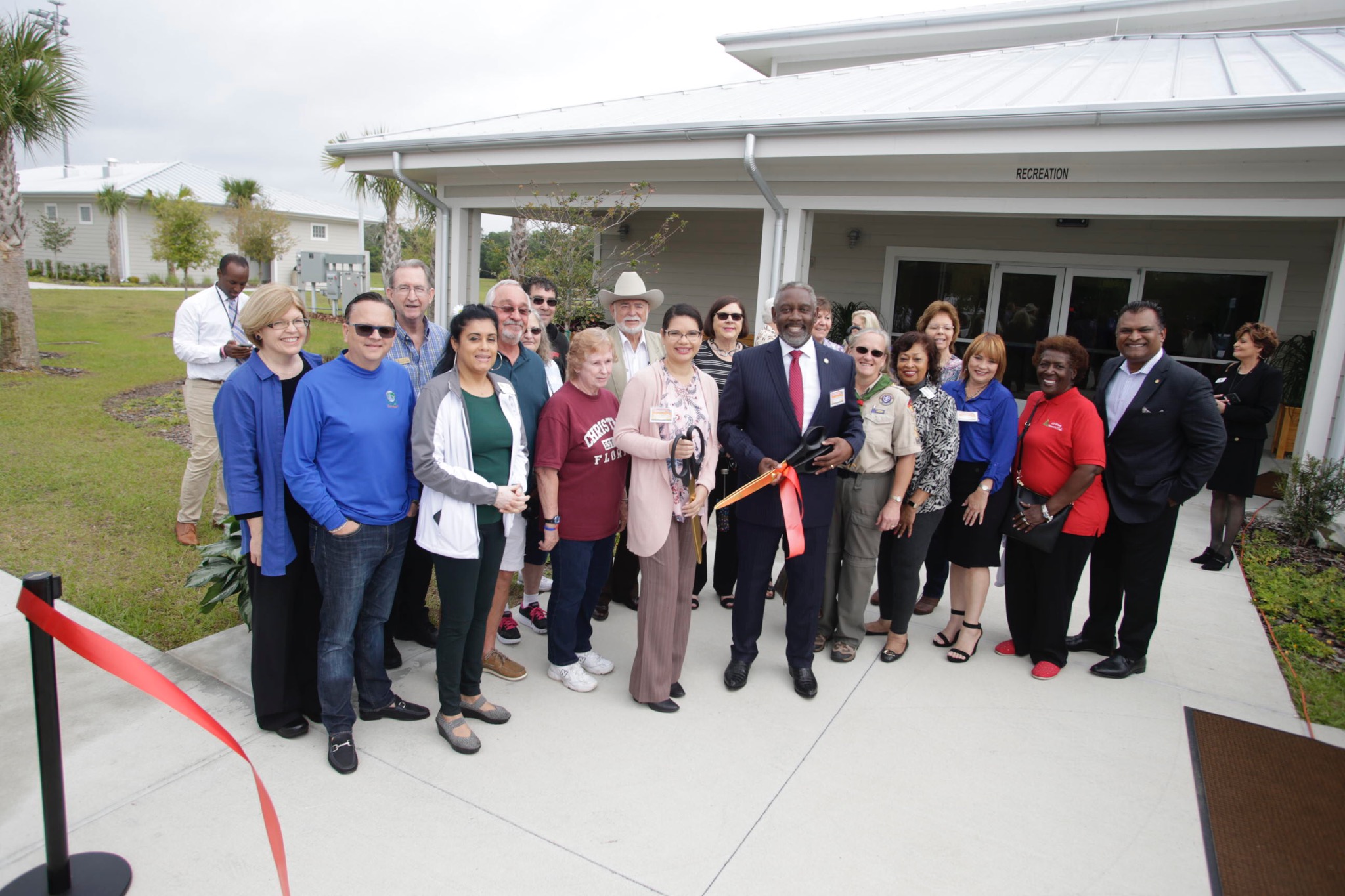 Mayor Demings, Commissioner Bonilla, Commissioner Gomez Cordero are joined by a dozen other individuals. They are standing for a photo and the Mayor is holding large scissors which he used to cut a ribbon.