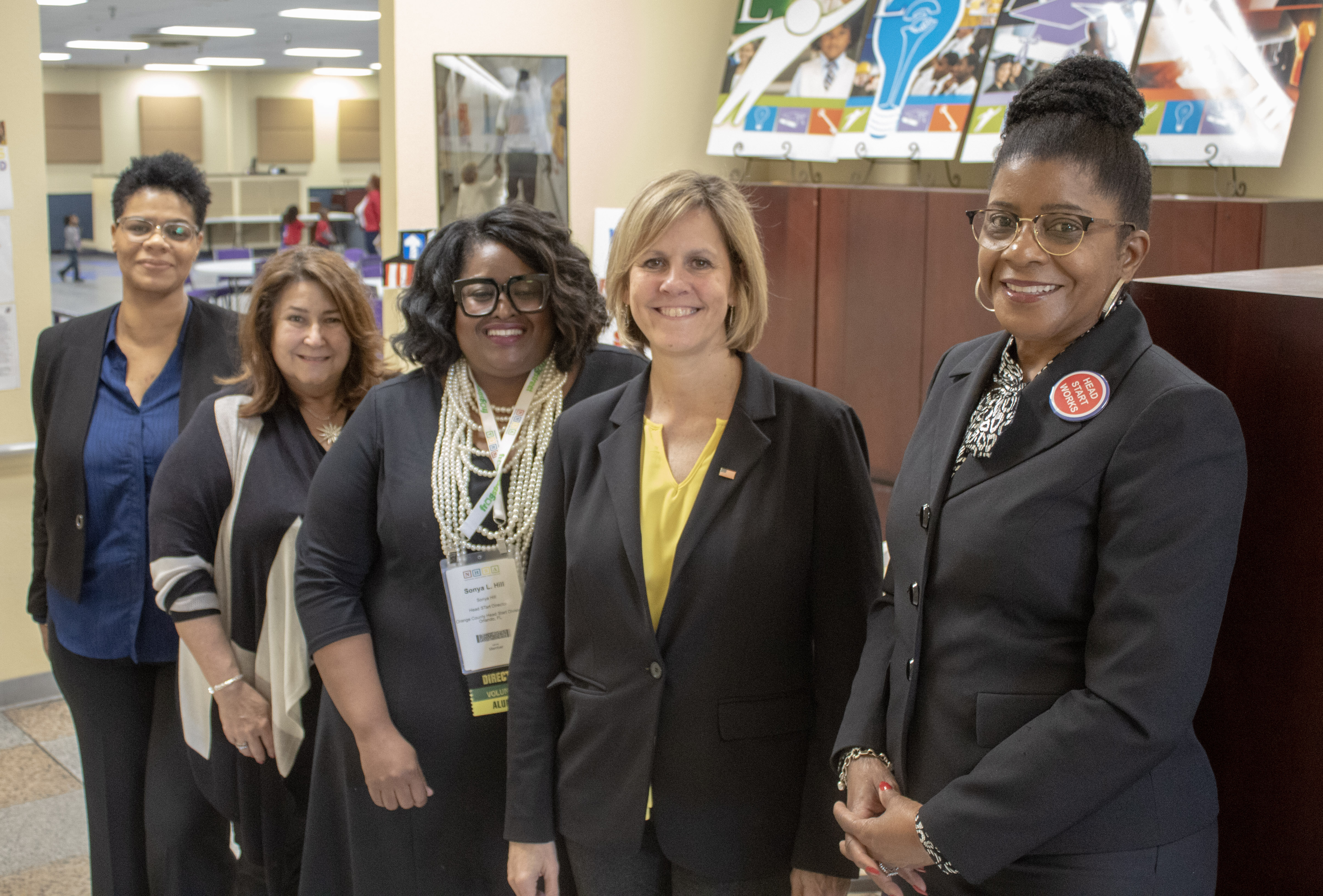 Five Head Start staff members, all women, standing in a diagonal line for a photo. They are smiling and are inside an office setting.