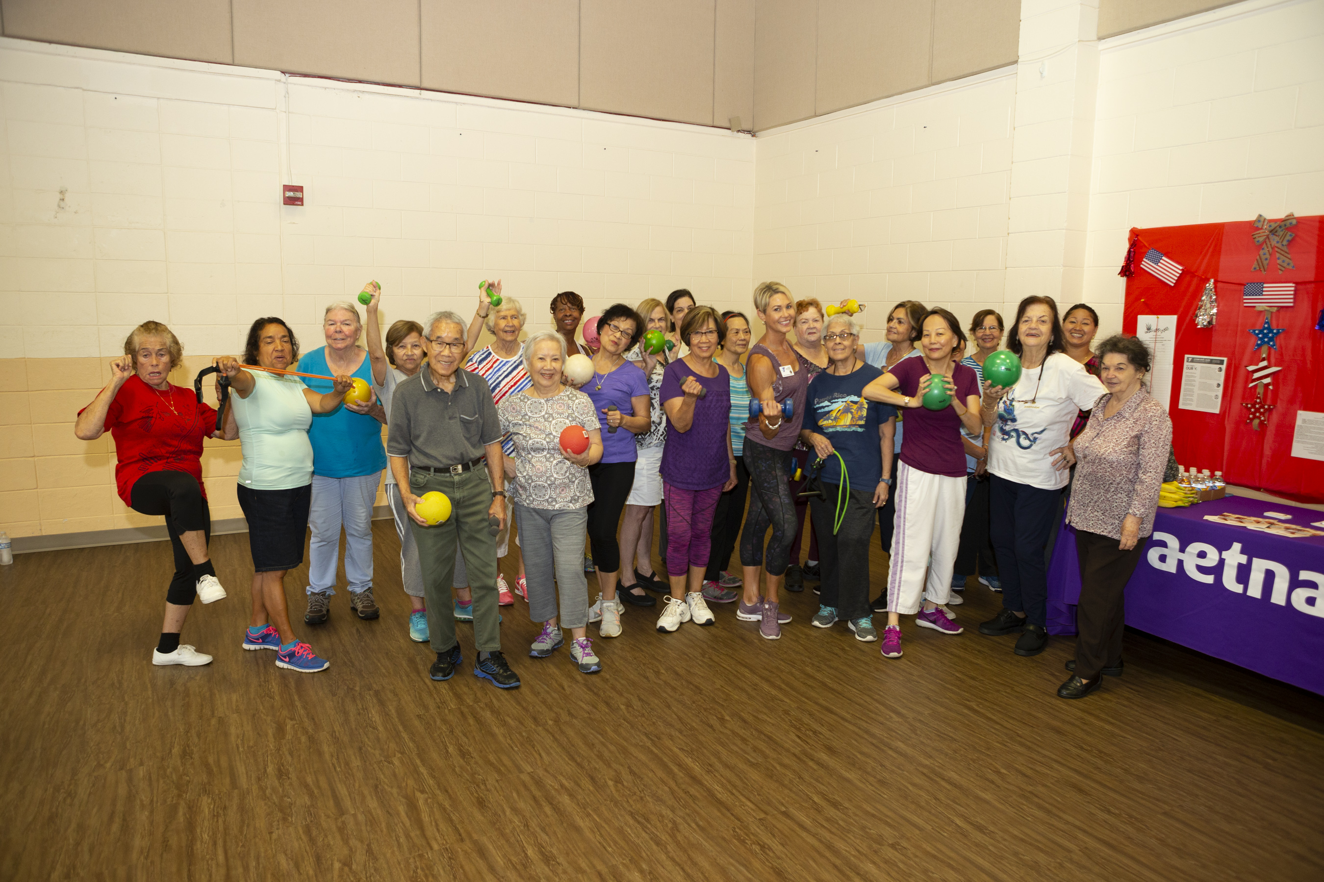 A group of senior citizens posing for a photo with their instructor as they hold exercise equipment