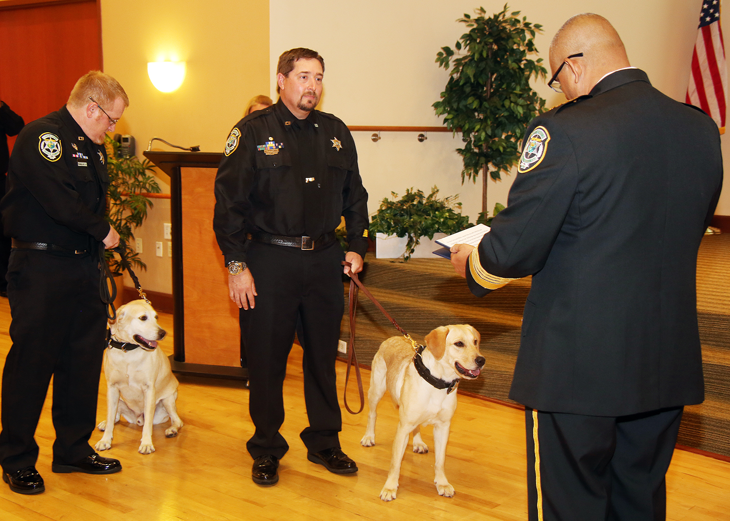 Two officers holding two K-9 dogs on a leash as they are sworn in