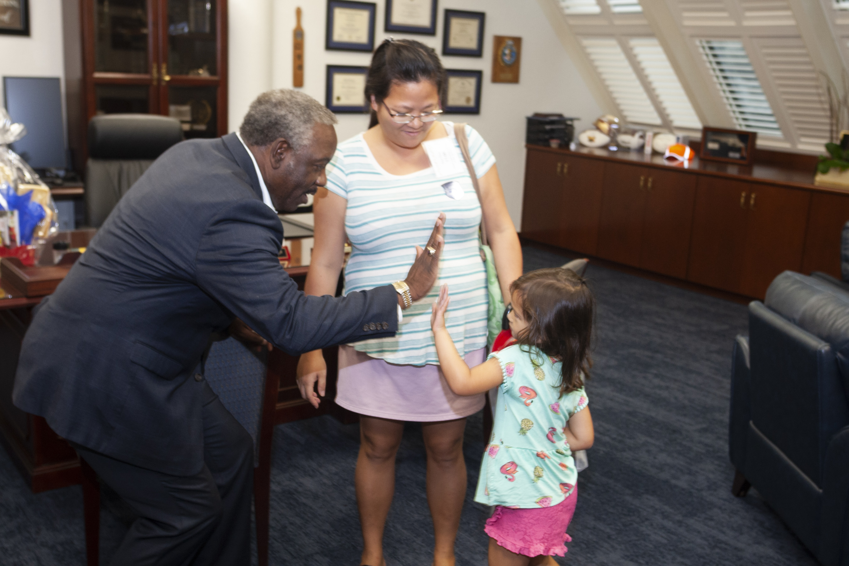 Mayor Demings giving a high-five to a little girl while her mother stands beside them. They are in the Mayor's office.