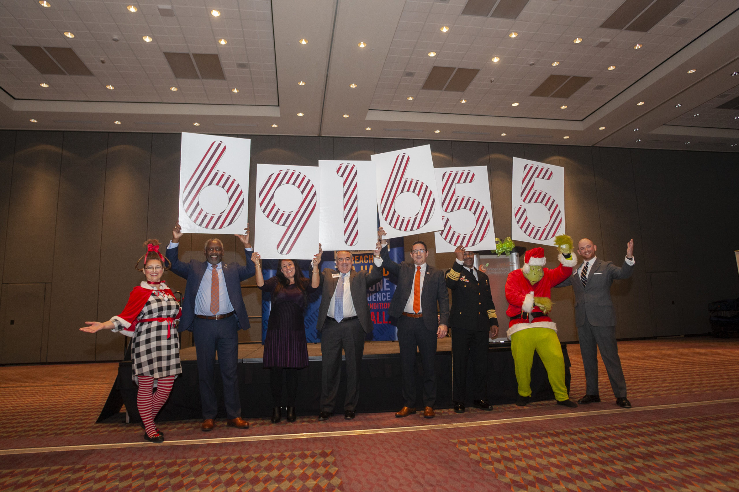 Business leaders holding signs with numbers on them representing a total number of fundraising dollars