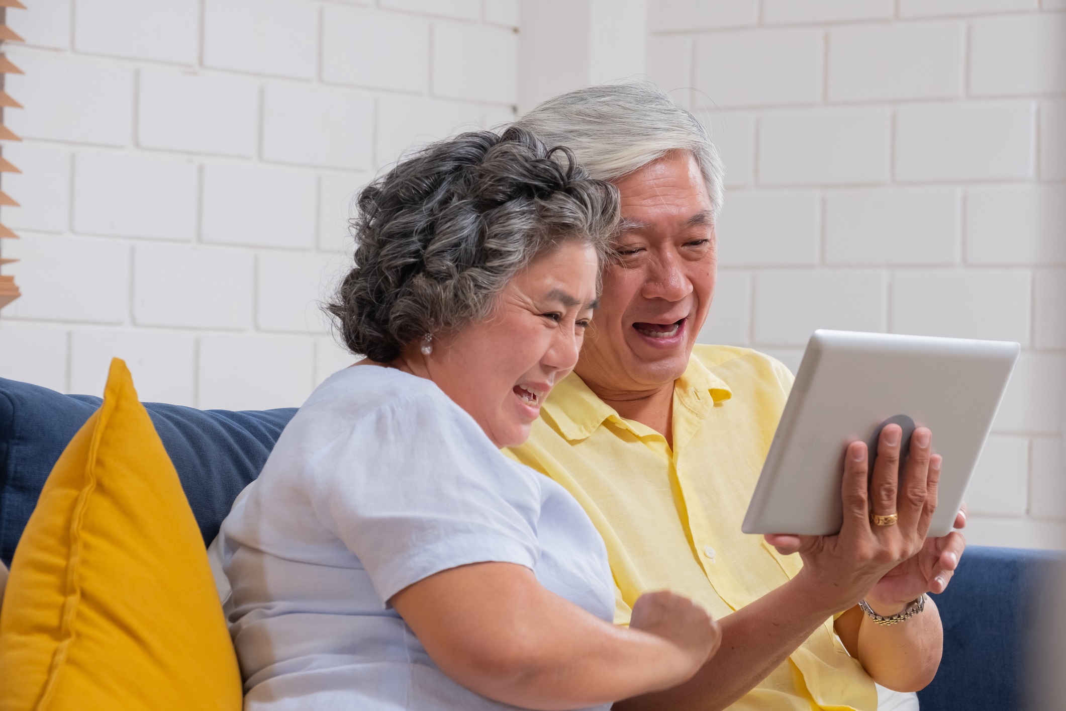 Una pareja asiática de la tercera edad usa una tablet para hacer una videollamada y hablar con su nieto.