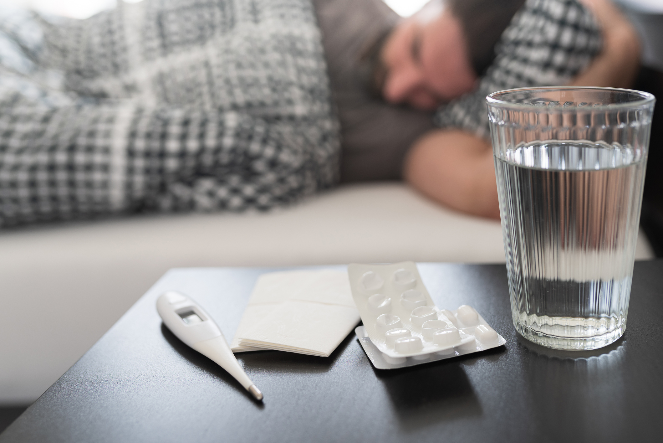 termómetro médico y un vaso de agua en la mesa de noche de una persona enferma de gripe o con resfriado común que duerme en la cama