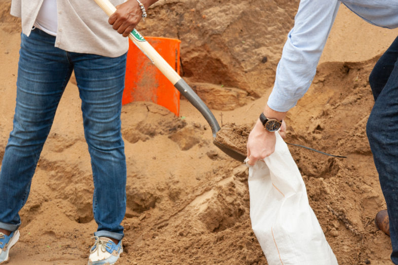 Two people shoveling sand into a bag to create a sandbag