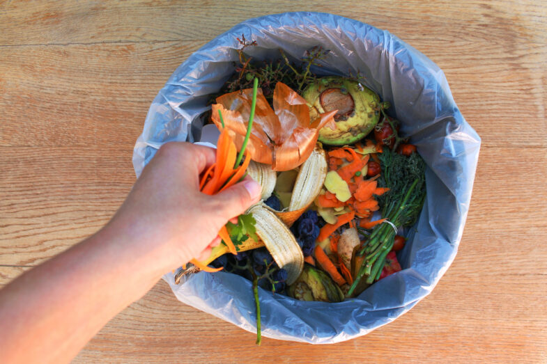Person drops food waste into a composting container.