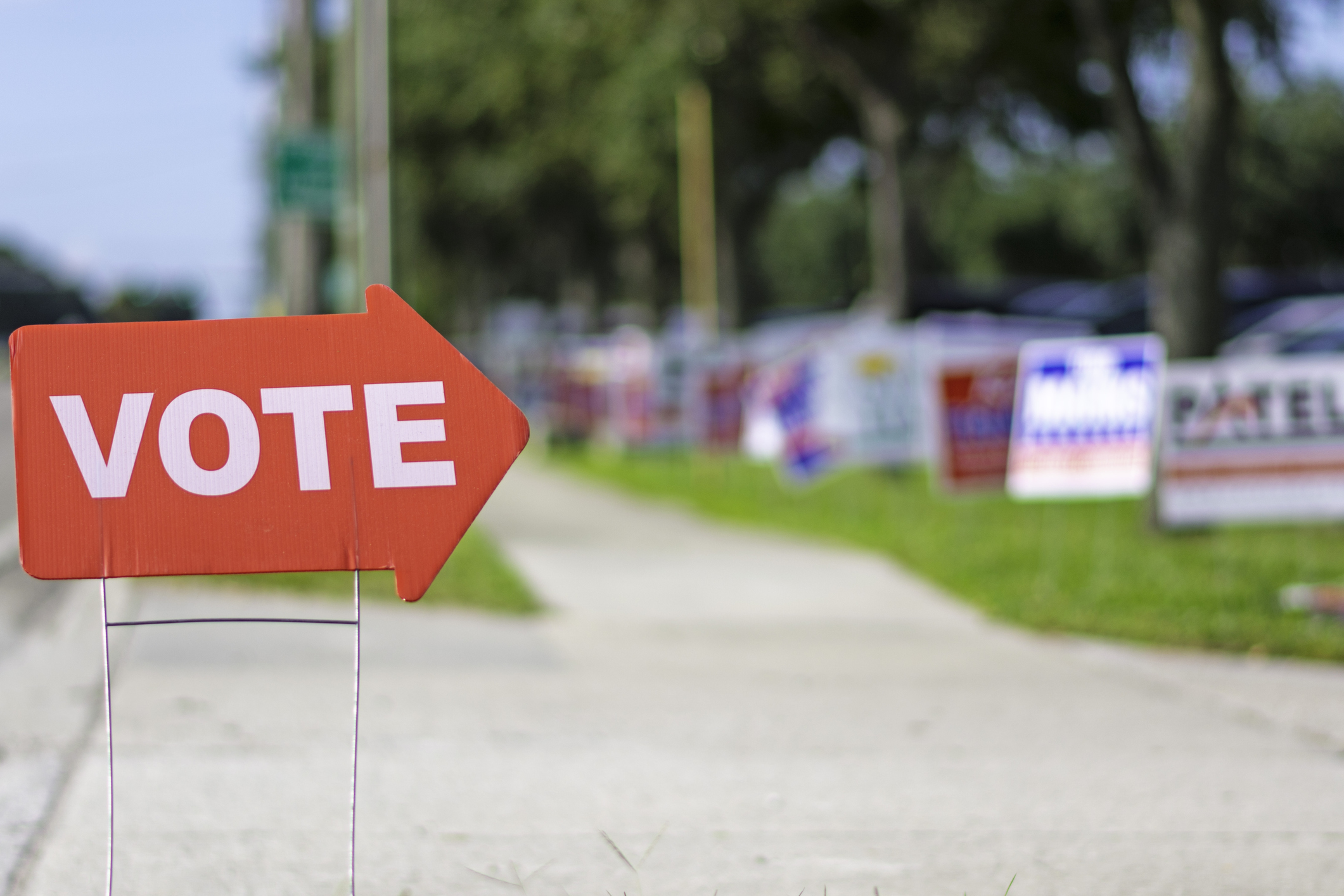 Cartel que indica a los votantes hacia dónde se encuentra el centro electoral, con carteles de partidos políticos de fondo