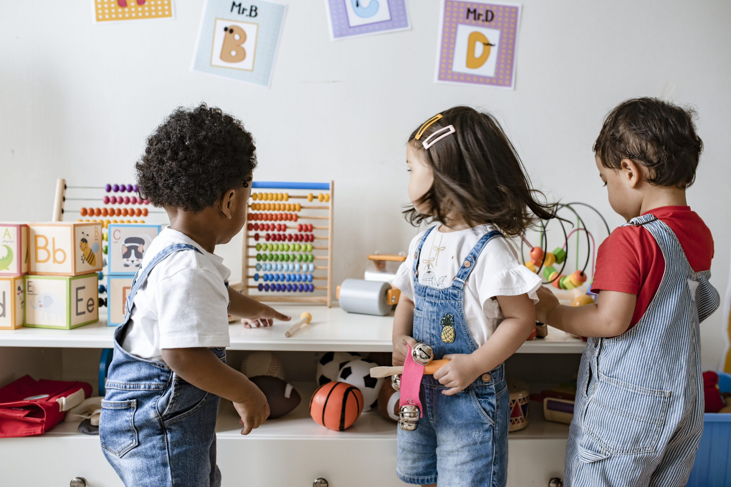 Three young children play with educational toys in a classroom setting.