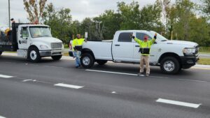 Two Orange County Public Works employees stand in front of their vehicles celebrating the completion of the Boggy Creek Road expansion project.