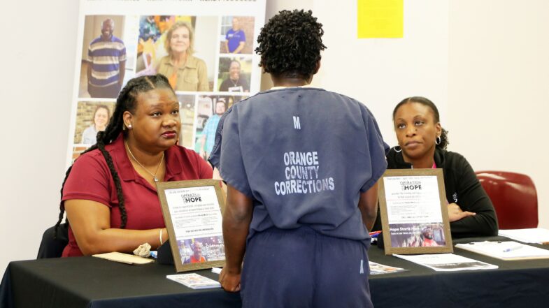 Standing inmate speaks with two representatives sitting at a table during a recent job fair.